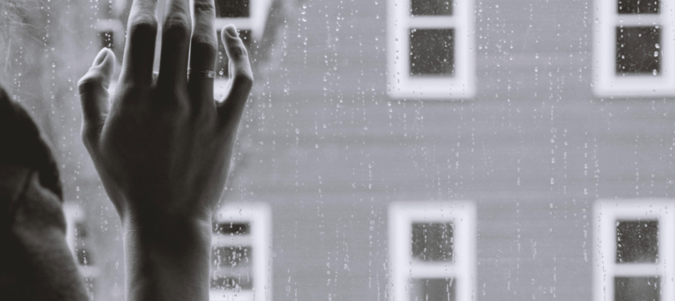 A mão da mulher encostada a uma janela chuvosa