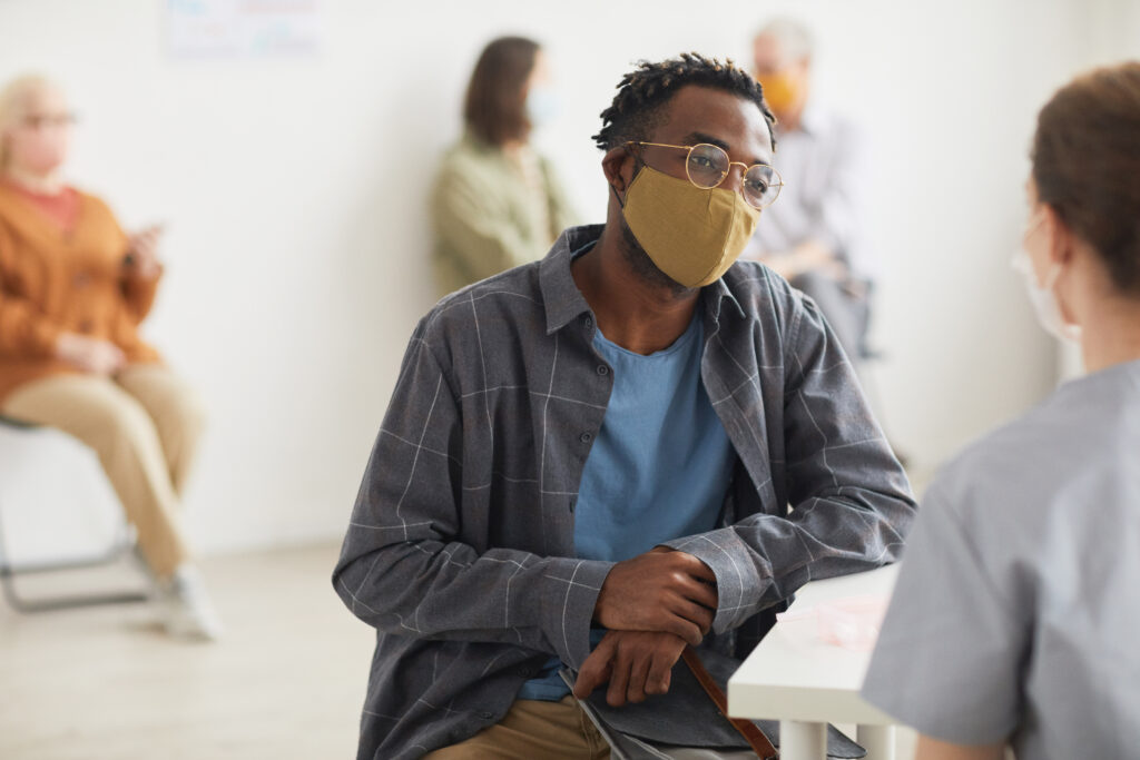 Young African American man wearing mask while talking to doctor