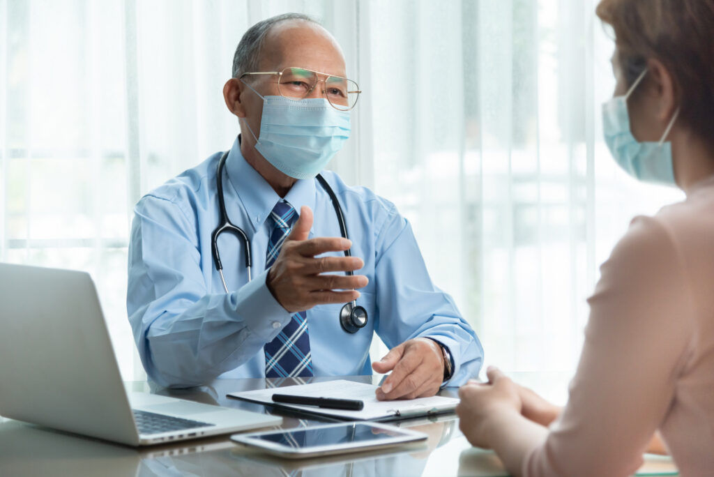 Asian male doctor wearing protective face mask talking with female patient