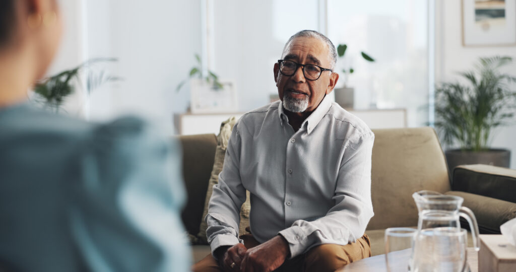 An older male client looks worried while talking to a psychologist.