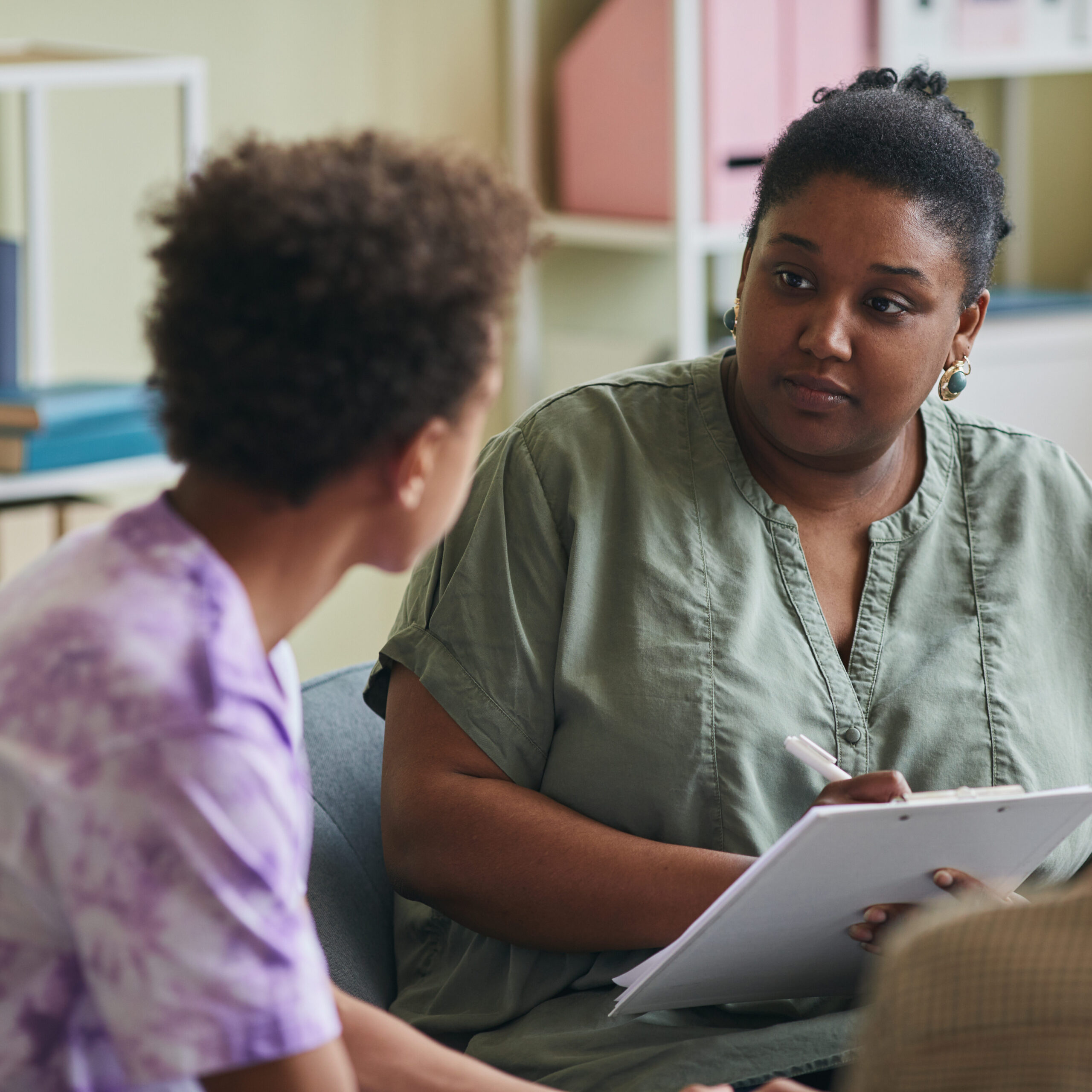 African American psychologist listening to teenage boy and making notes
