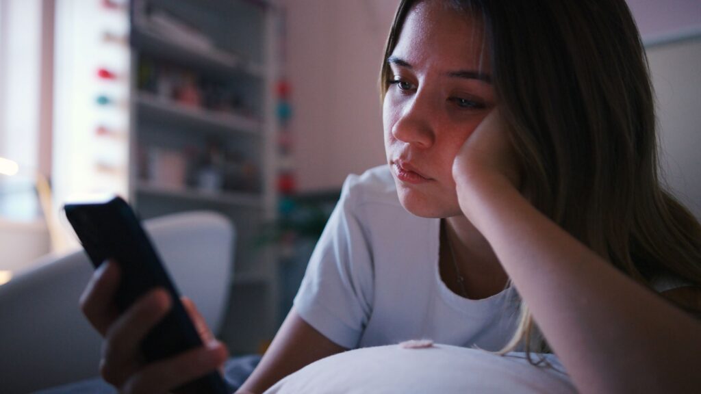 Young adult looking at her phone looking sad.