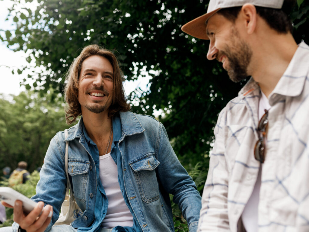 Two men talk in a park, looking happy and empowered.